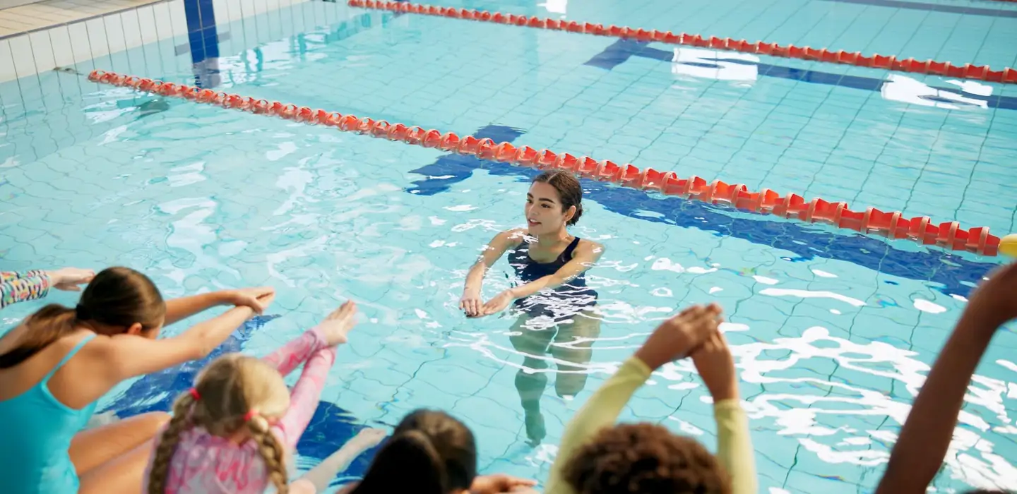 Swimming instructor guiding a group of children during a pool lesson.