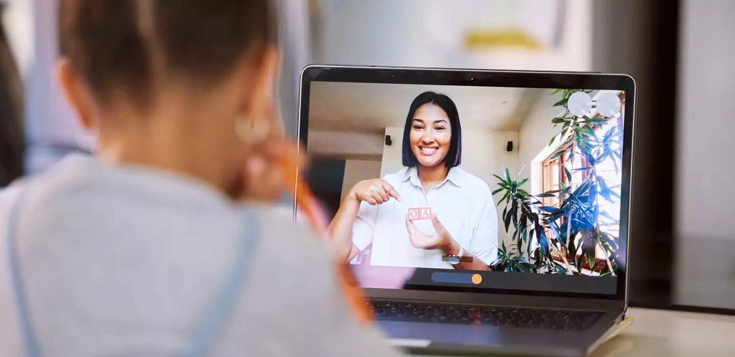 Child watching an online tutor on a laptop during a video lesson.