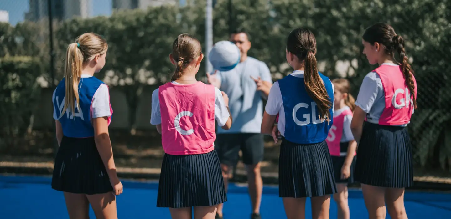 Netball coach demonstrating a drill to a group of young players outdoors.