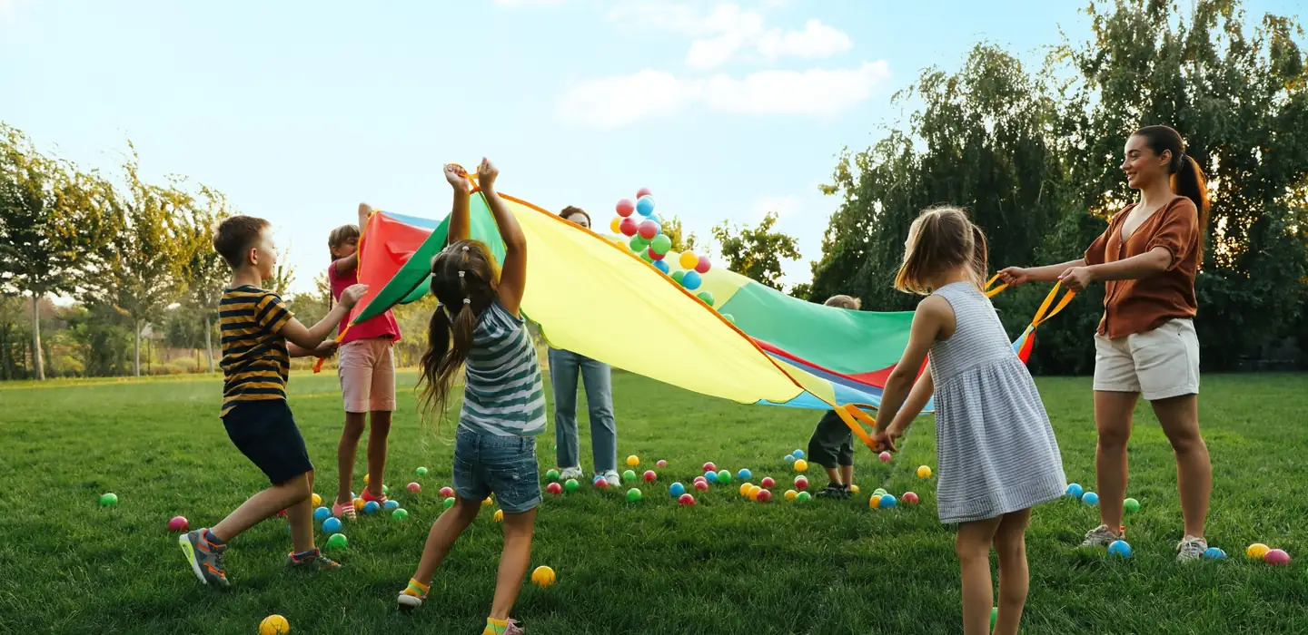 Children playing together outdoors with a colourful parachute at a holiday camp.