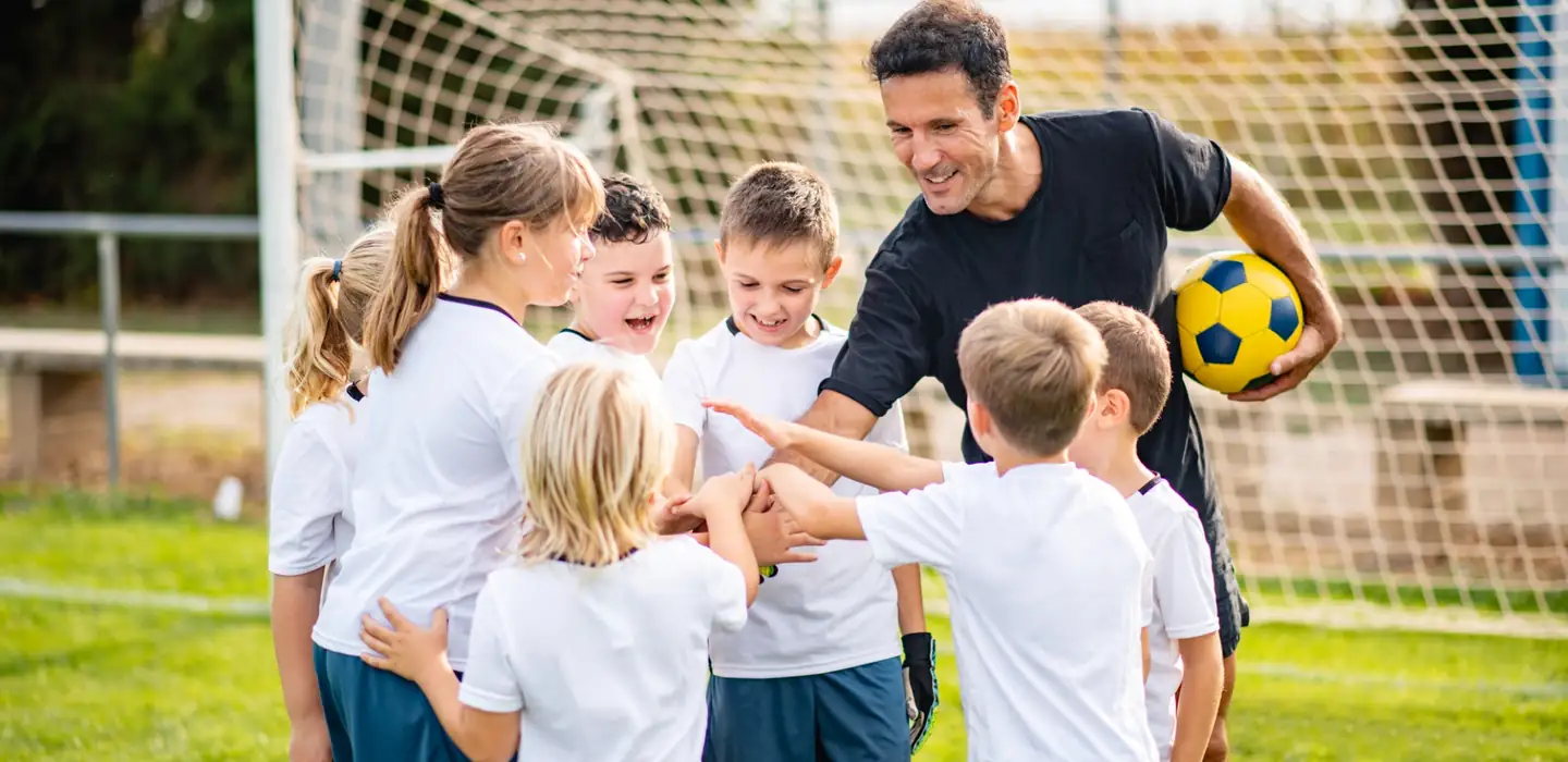 Football coach encouraging a group of young children during a training session.
