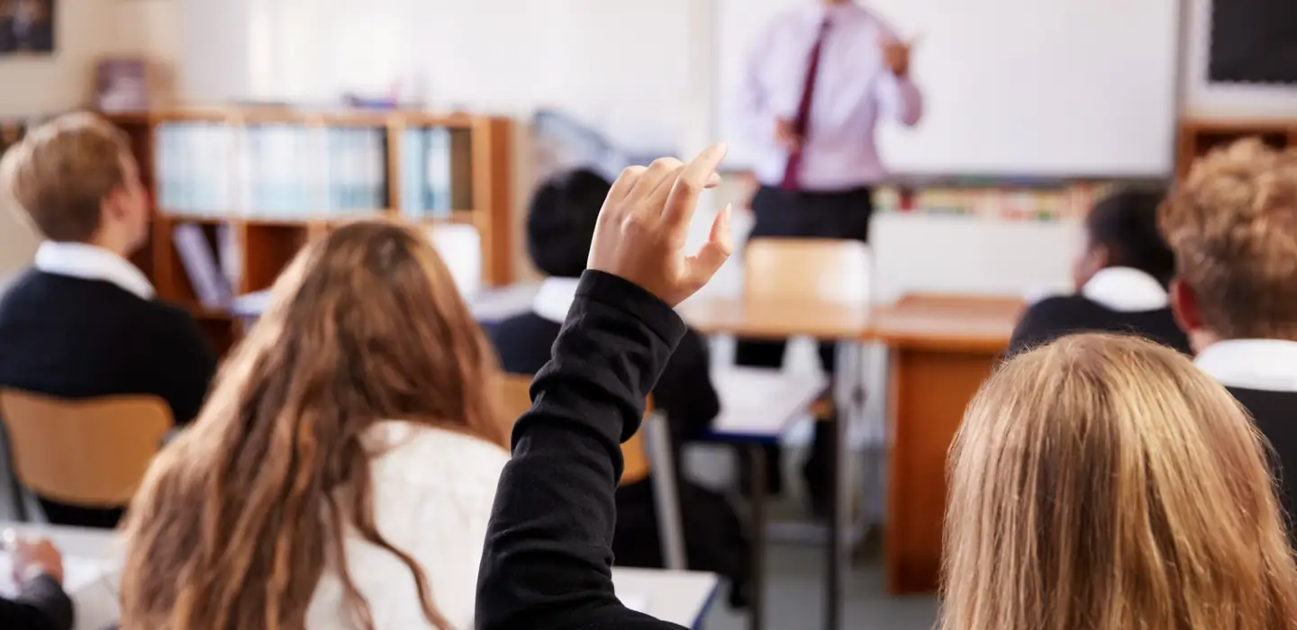 Student raising their hand to answer a question in a classroom.