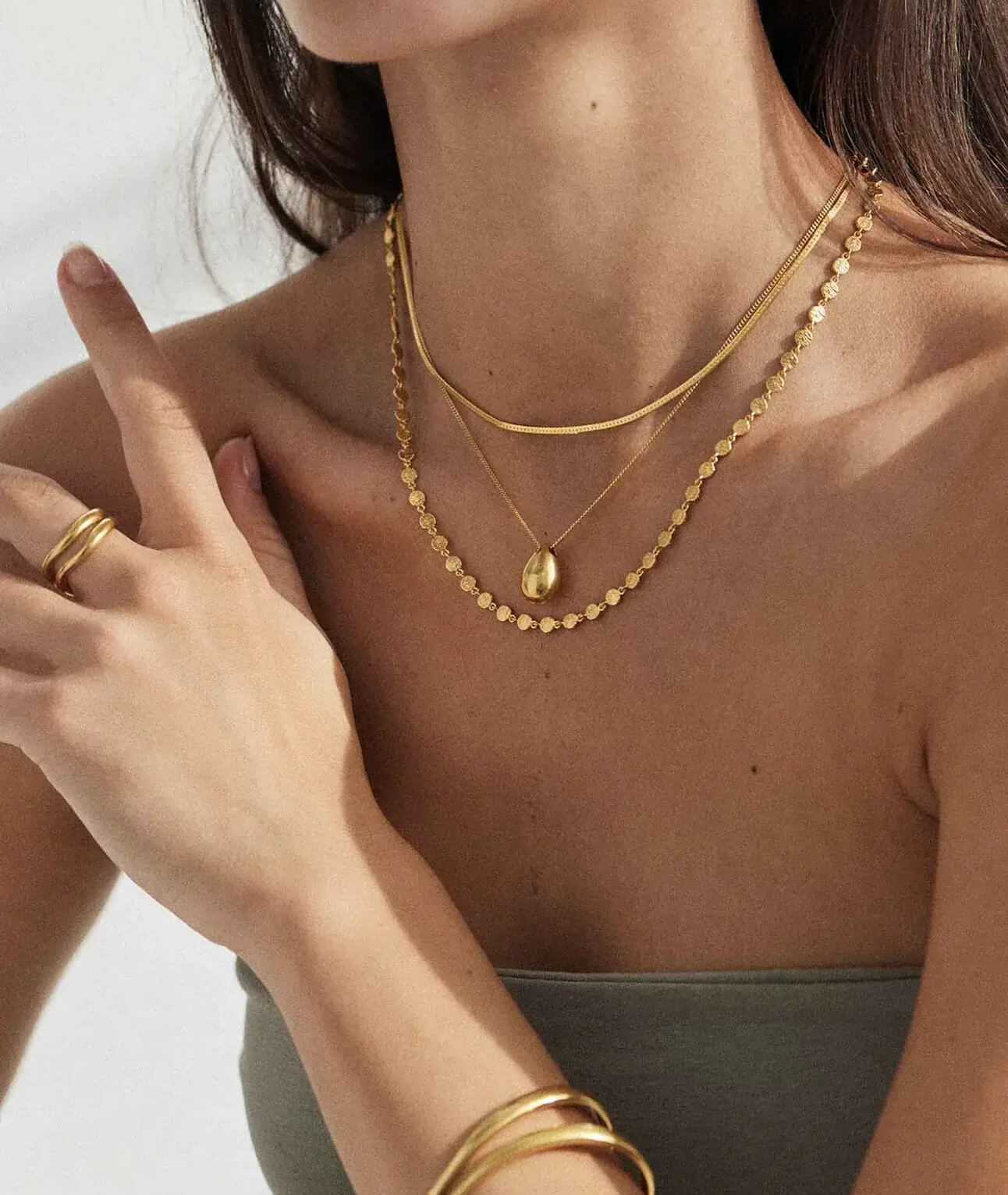 Woman wearing layered gold necklaces, gold rings, and gold bracelets with a sleeveless top.
