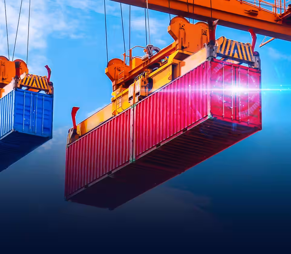 Red and blue shipping containers suspended by orange cranes against a blue sky.