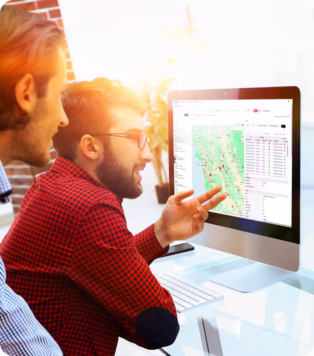 Two men looking at a computer screen displaying a map with location markers and data tables.
