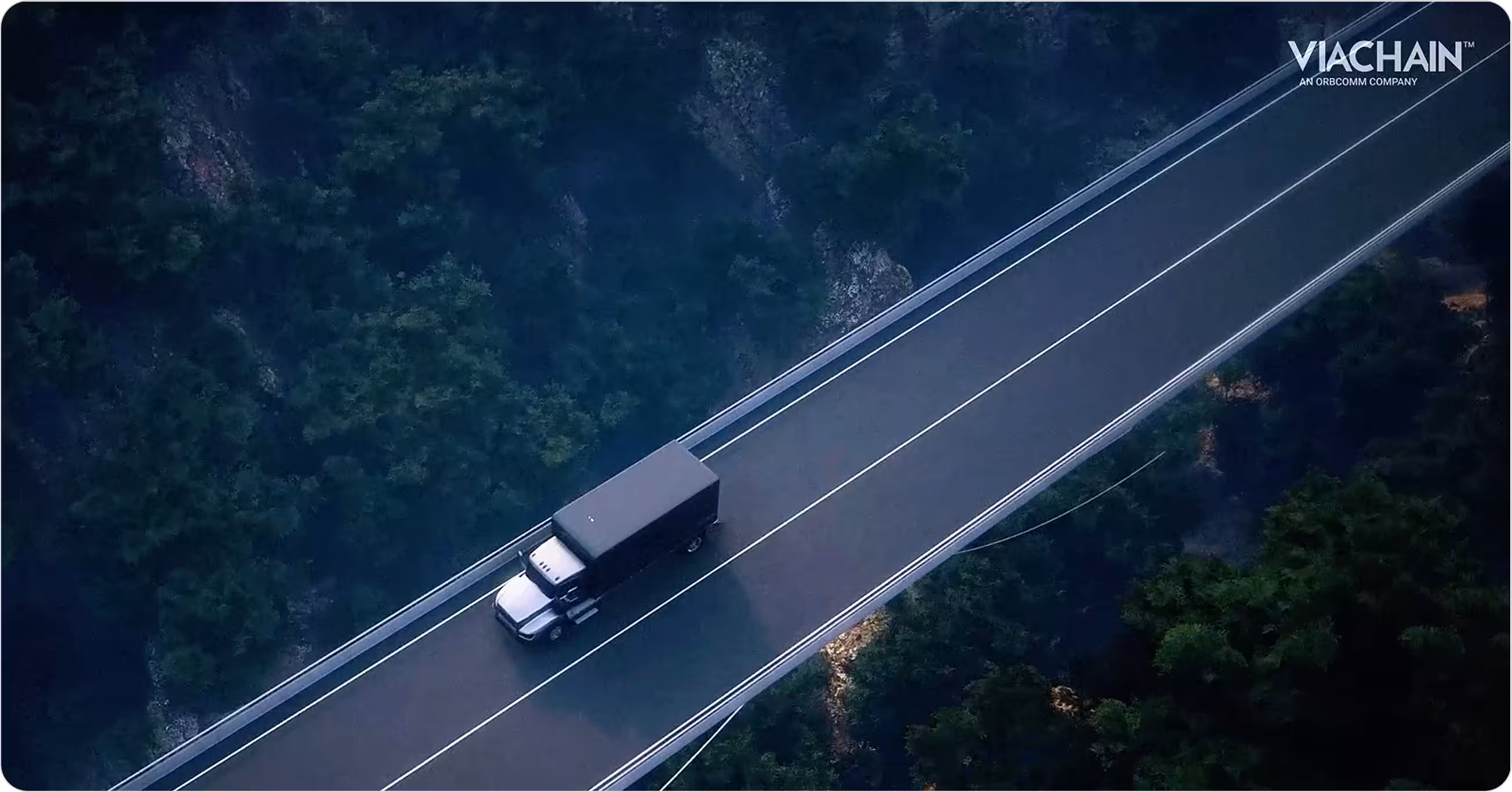 Um caminhão de entrega preto dirigindo em uma rodovia elevada cercada por uma floresta densa, com o logotipo da ViaChain no canto superior direito.