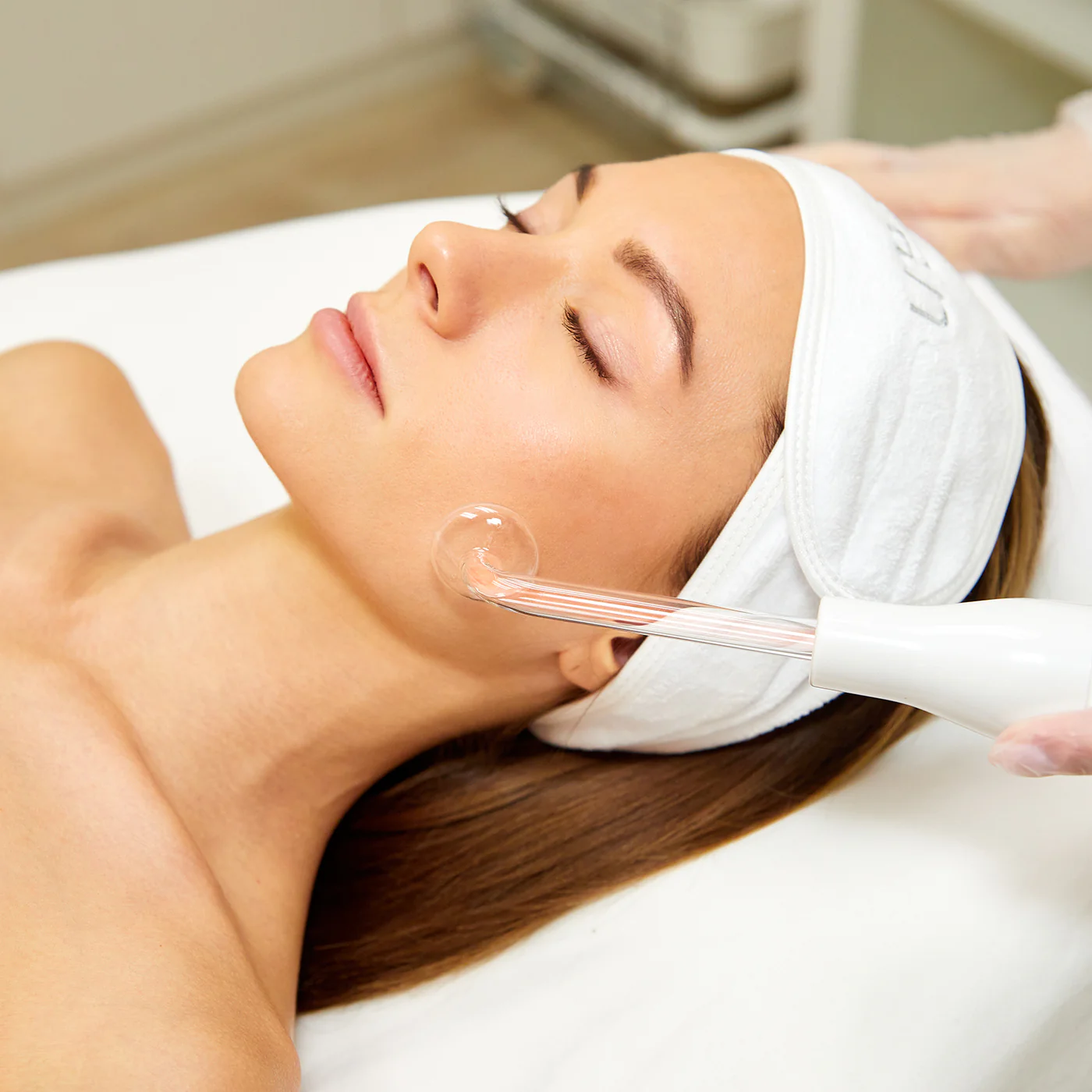 Schöne junge Frau liegt auf einem Liegestuhl und lässt sich mit einem Hochfrequenzgerät im Gesicht behandeln.
