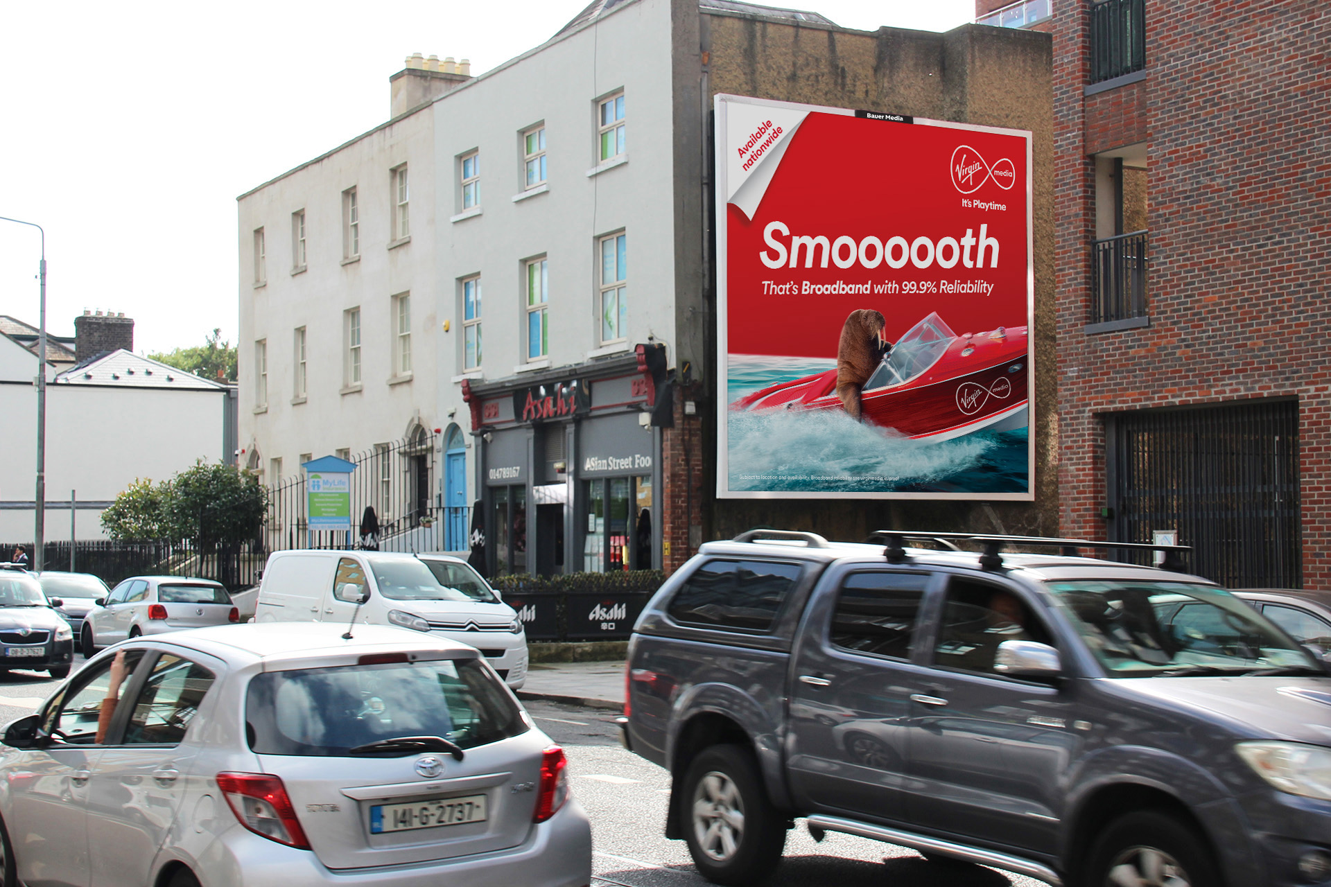 Bauer Media Outdoor digital advertising billboard on a residential roadside displays a leasing.com ad with the message "Say goodbye to buying," as cars and a cyclist pass by.