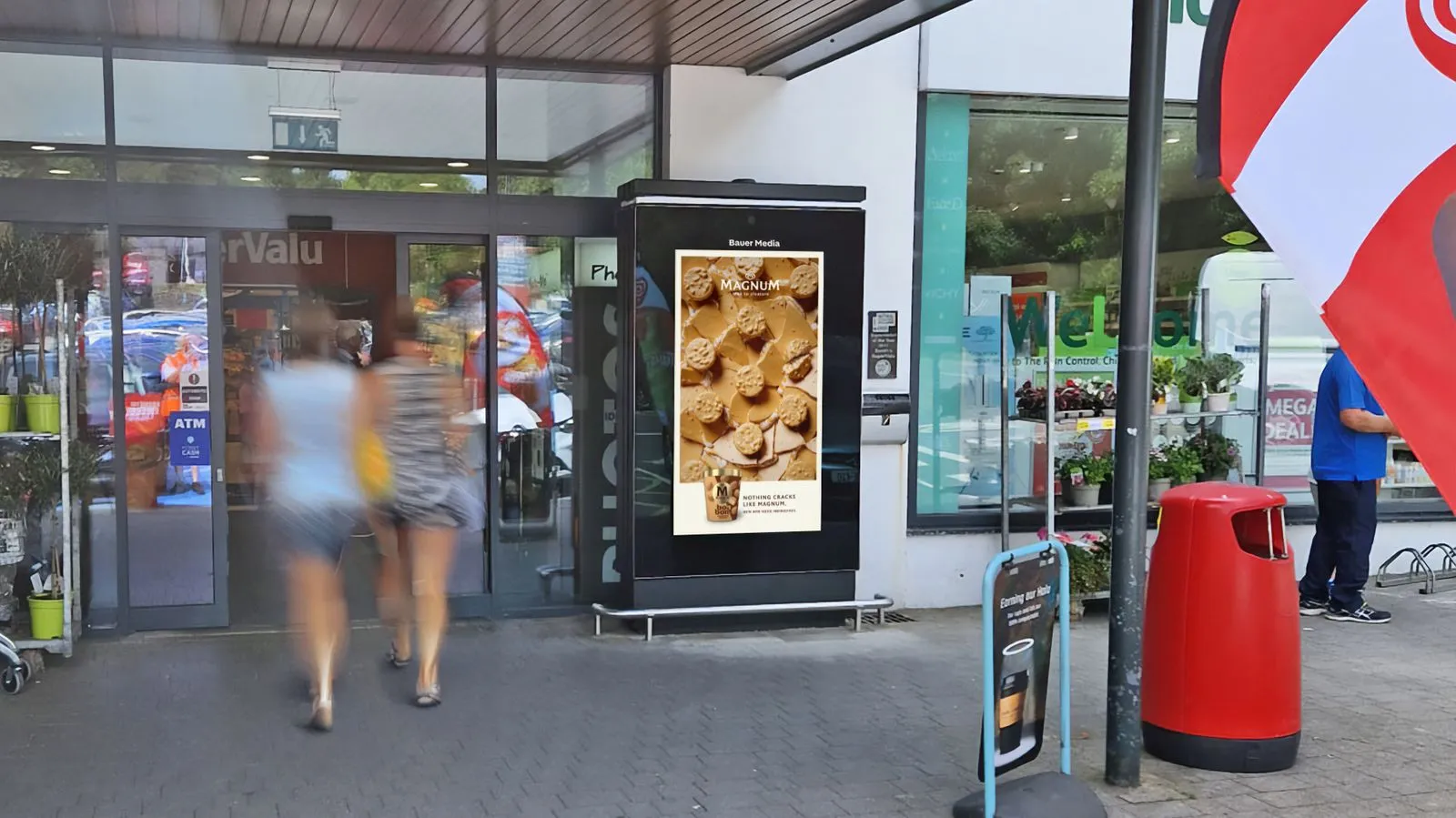 Digital advertisement outside of a Supervalu entrance with shoppers walking by