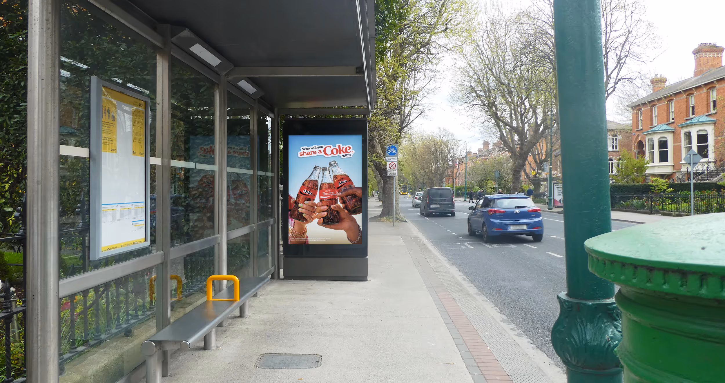 An Adshel 6-Sheet bus shelter displaying an advertisement for Coke, on a leafy Dublin City street