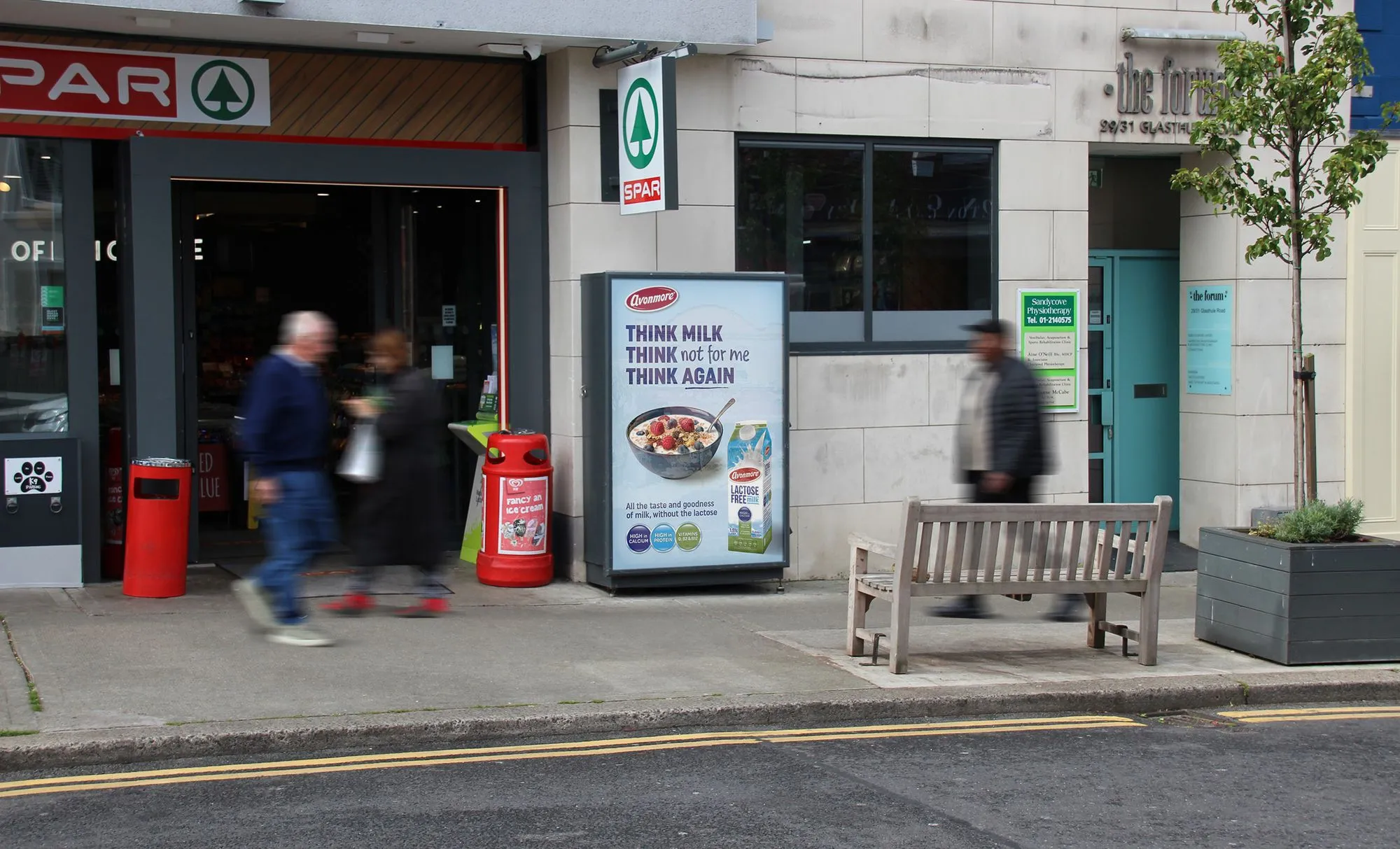 An Adbox 6-Sheet poster unit displaying an advertisement for Avonmore Lactose-Free milk, situated outside of the entrance of a Spar convenience store