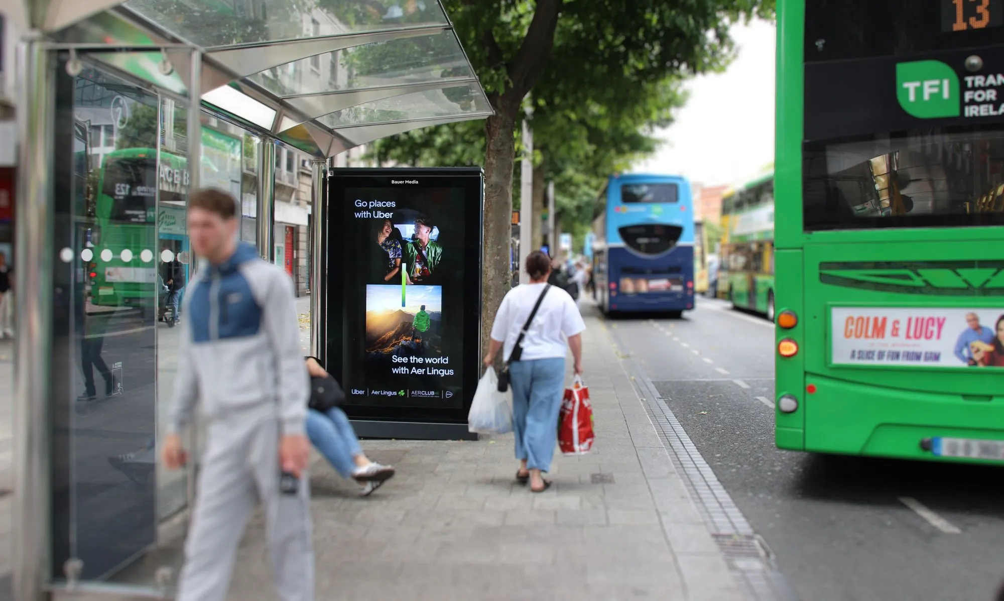 An Adshel Live bus shelter displaying an advertisment for Uber & Aer Lingus partnership, situated in a busy city centre environment in Dublin City