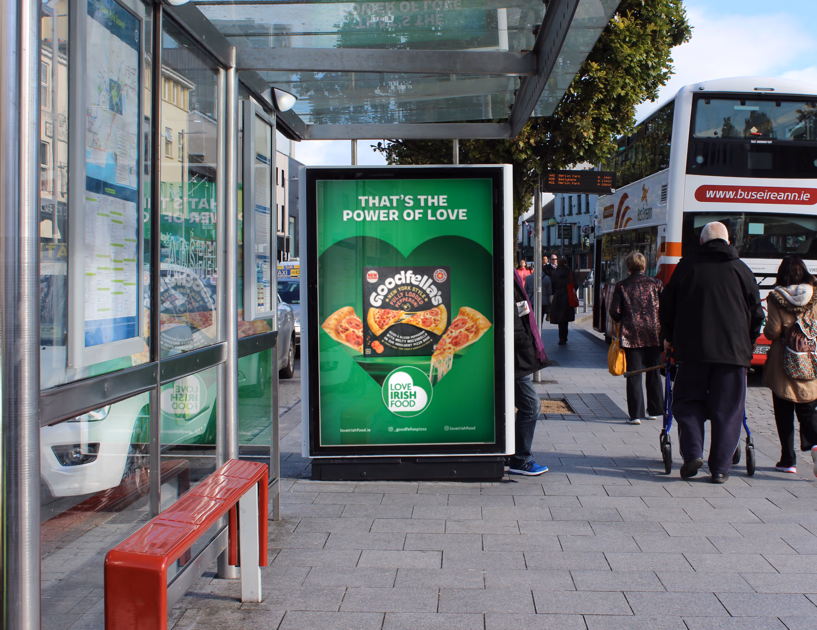 An Adshel bus shelter at a busy bus terminus displaying a poster for Goodfellas Pizza