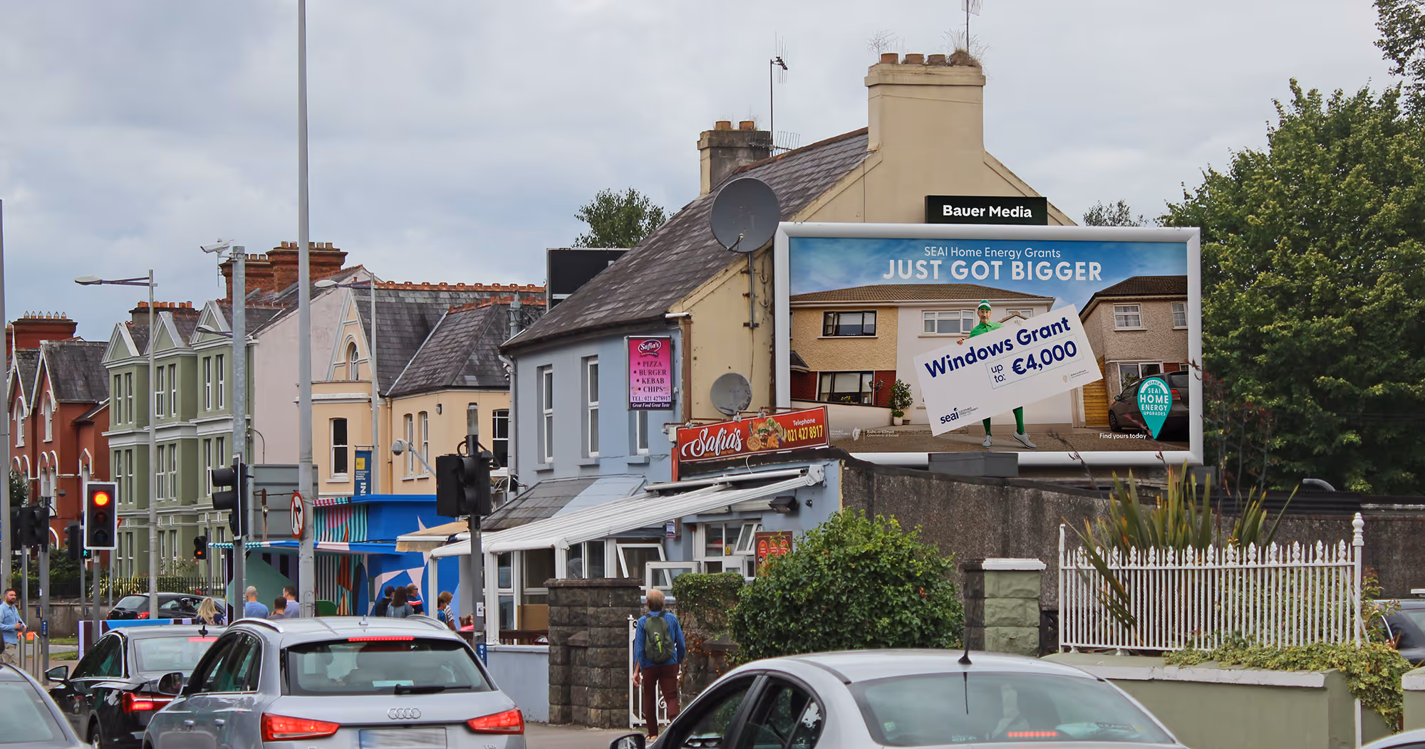 Bauer Media Outdoor digital advertising billboard on a residential roadside displays a leasing.com ad with the message "Say goodbye to buying," as cars and a cyclist pass by.