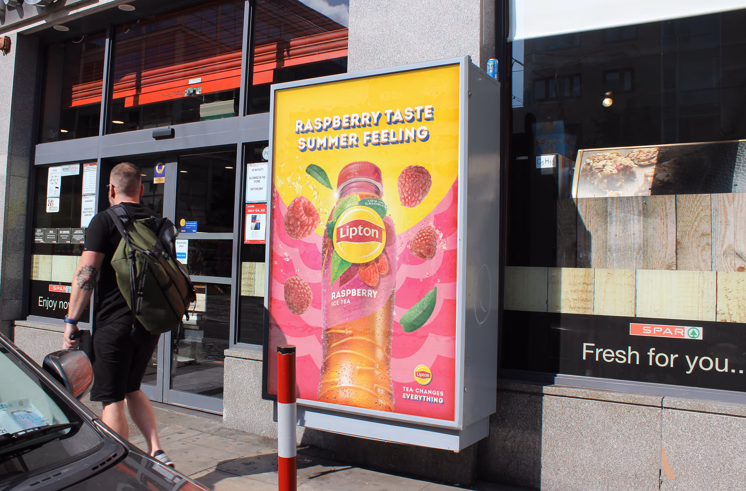 An Adbox at a convenience store entrance displaying a poster for Lipton Ice Tea