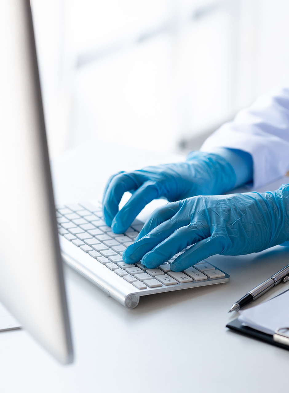 Ontwerper met medische handschoenen werkt aan logoherstel op Mac-toetsenbord — De LogoDokter, specialist in scherp en gezond merkbeeld.