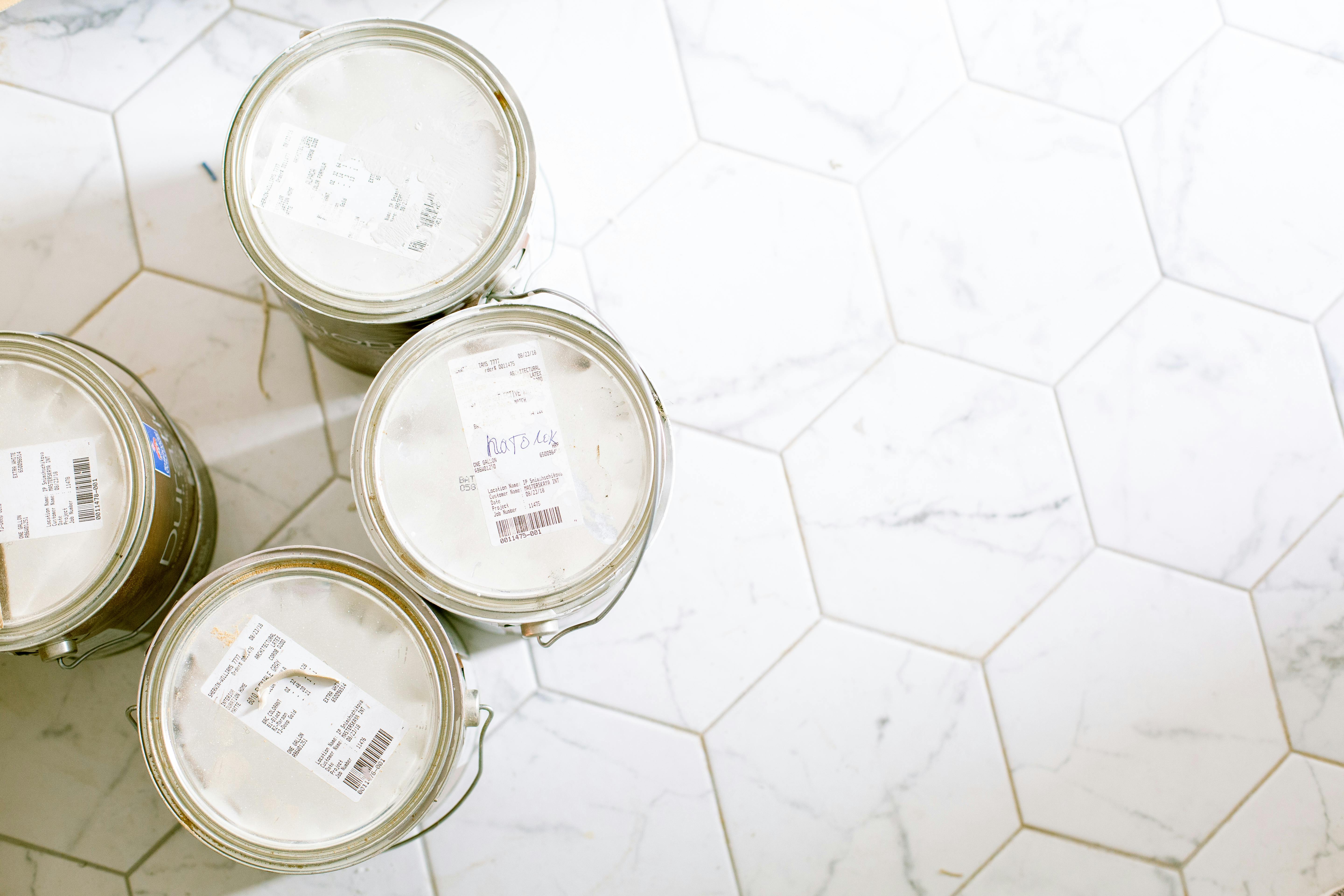 Four closed paint cans grouped together on a white hexagonal tiled floor.