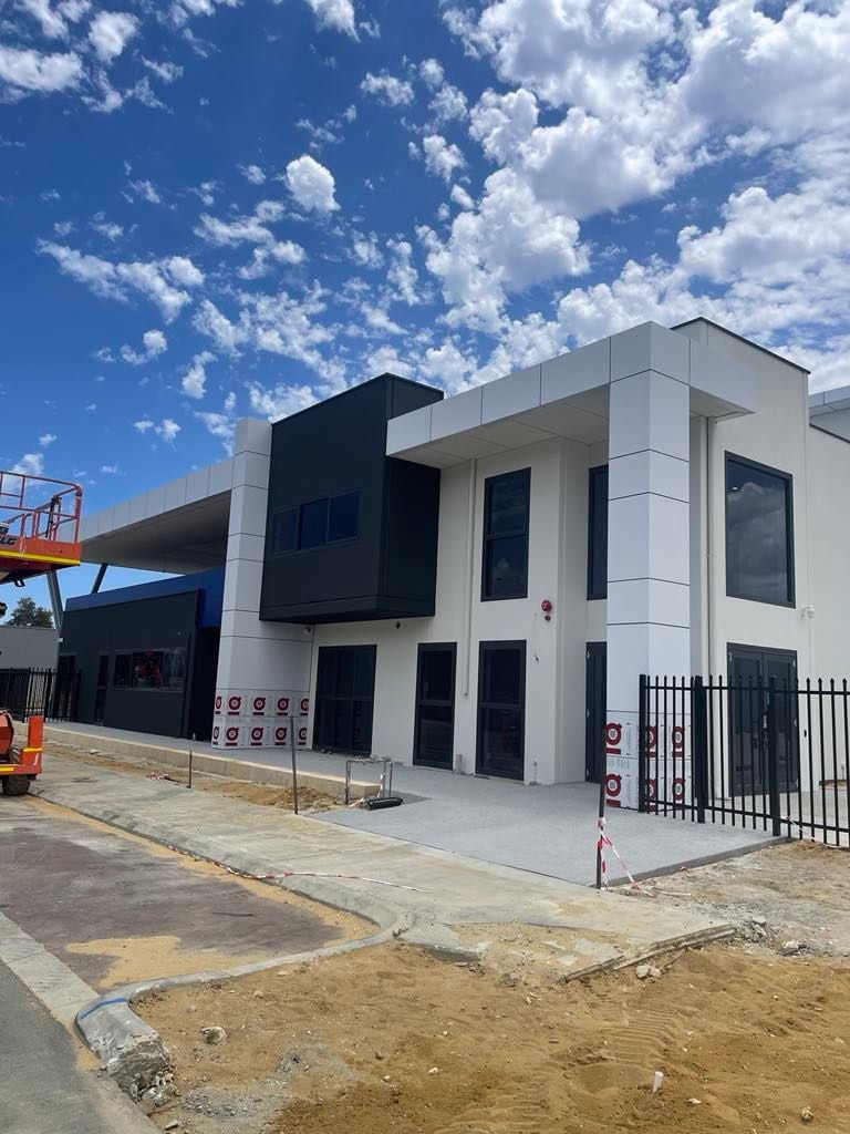 Modern commercial building under construction with black and white exterior panels, large windows, and a clear sky with scattered clouds.