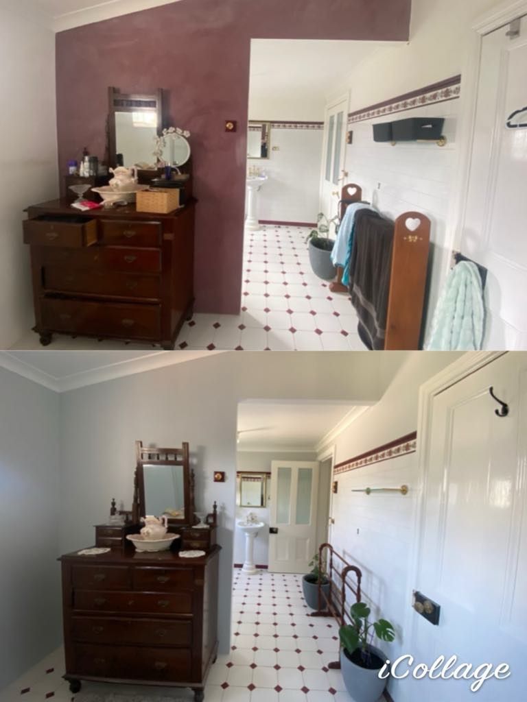 Vintage wooden dresser with mirror and wash basin in a bright bathroom with white tiled floor featuring red diamond patterns and plants.