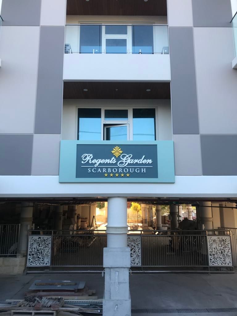Modern apartment building facade with a sign reading 'Regents Garden Scarborough' above a gated entrance and central pillar.