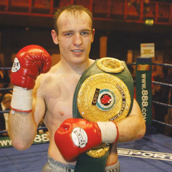 Former professional boxing champion Brian Magee holding title belt in the ring at Magee Health & Fitness gym Belfast