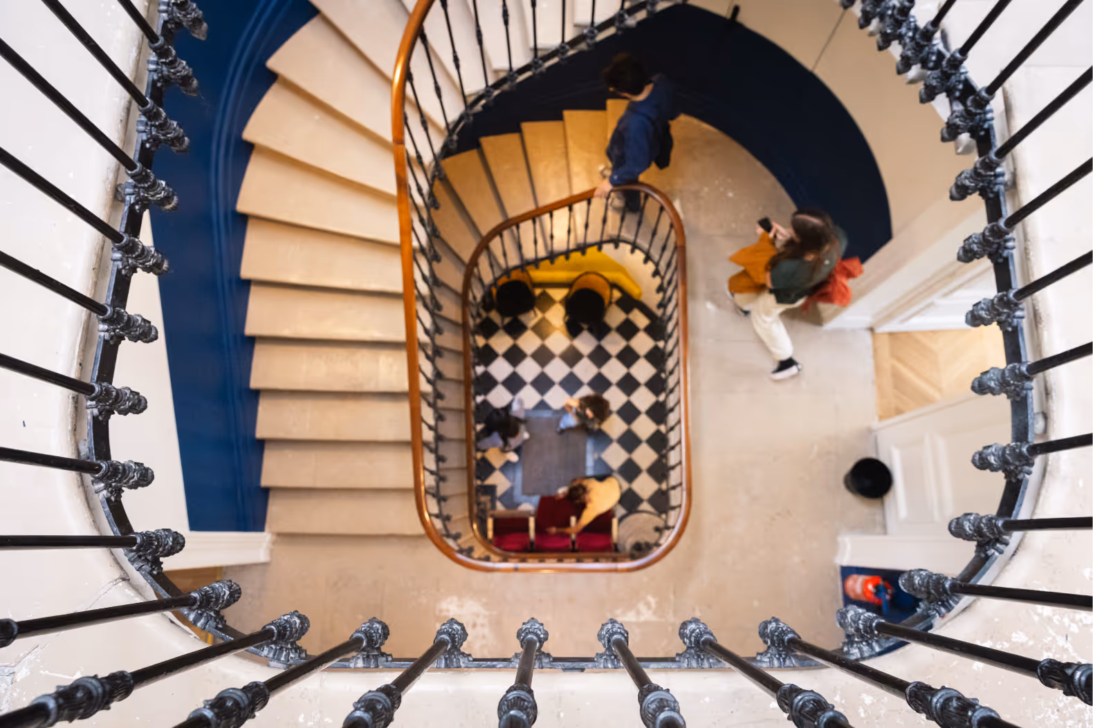 Vue plongeante sur le hall et l'escalier à vis (ou hélicoïdal) historique de l'École du Septième Art. On aperçoit des étudiants au bas de l'escalier, sur un sol en damier noir et blanc.