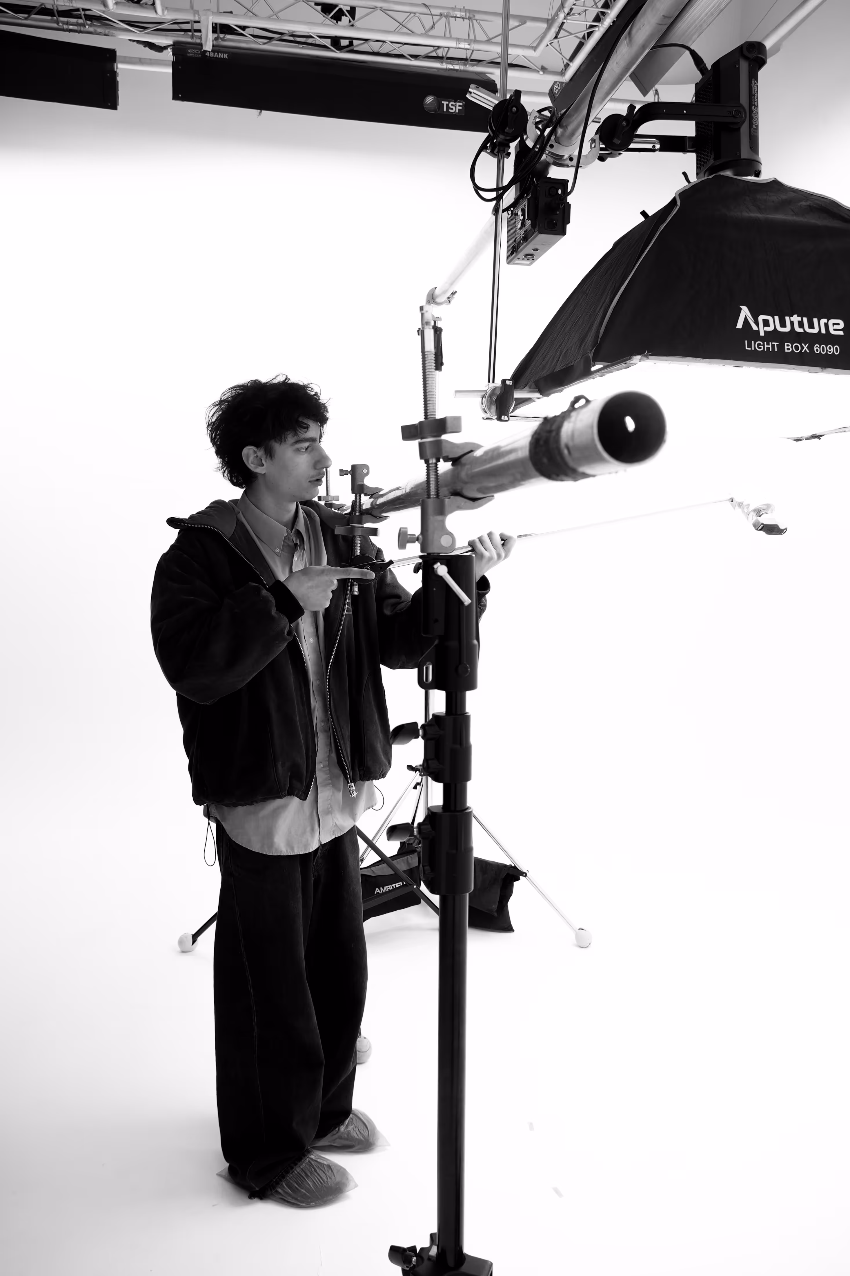 Homme dans un studio photo ajustant un équipement d'éclairage suspendu avec une boîte à lumière Aputure.