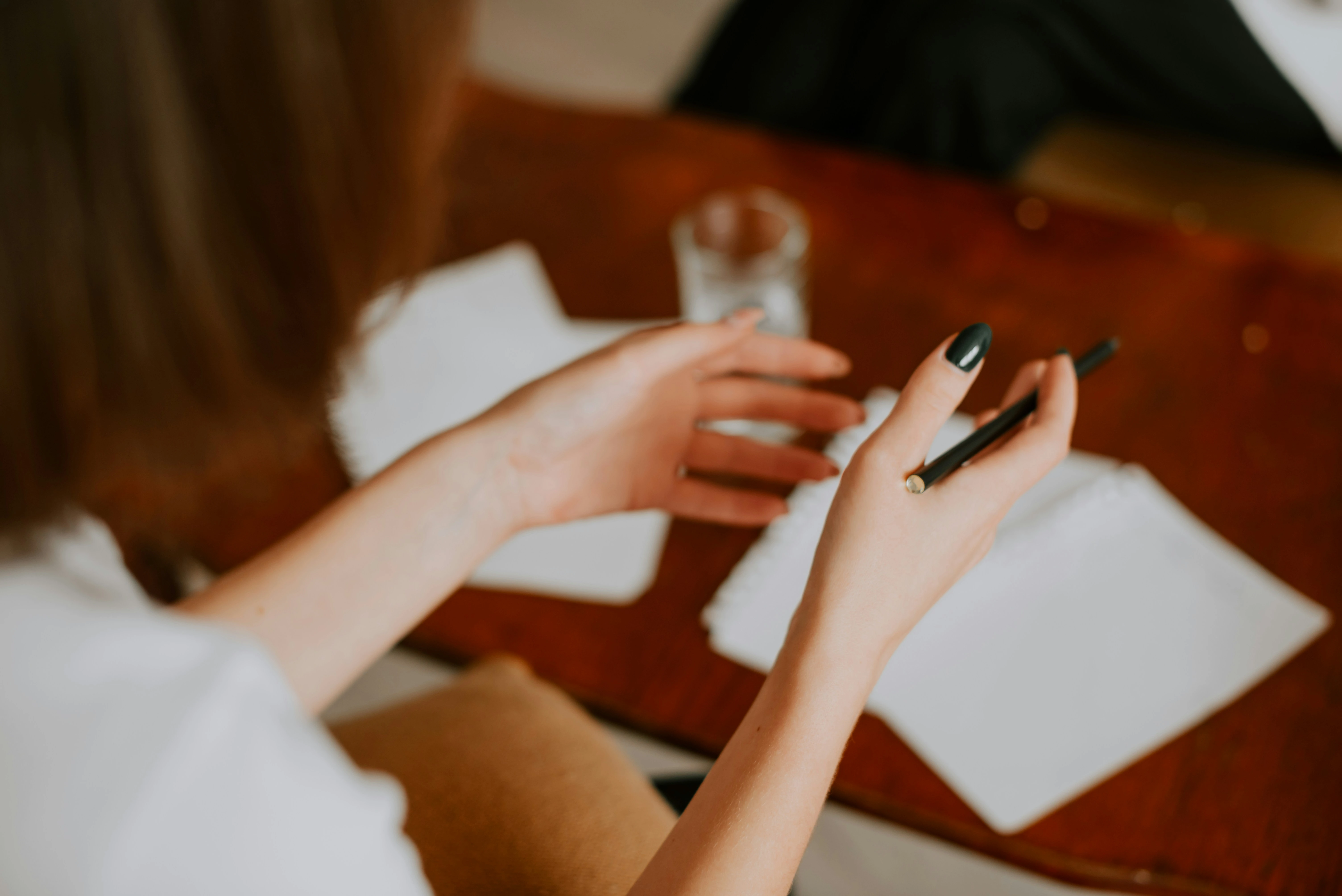 Overhead view of person writing in notebook at wooden desk with pen, cup of coffee, and papers scattered around workspace.