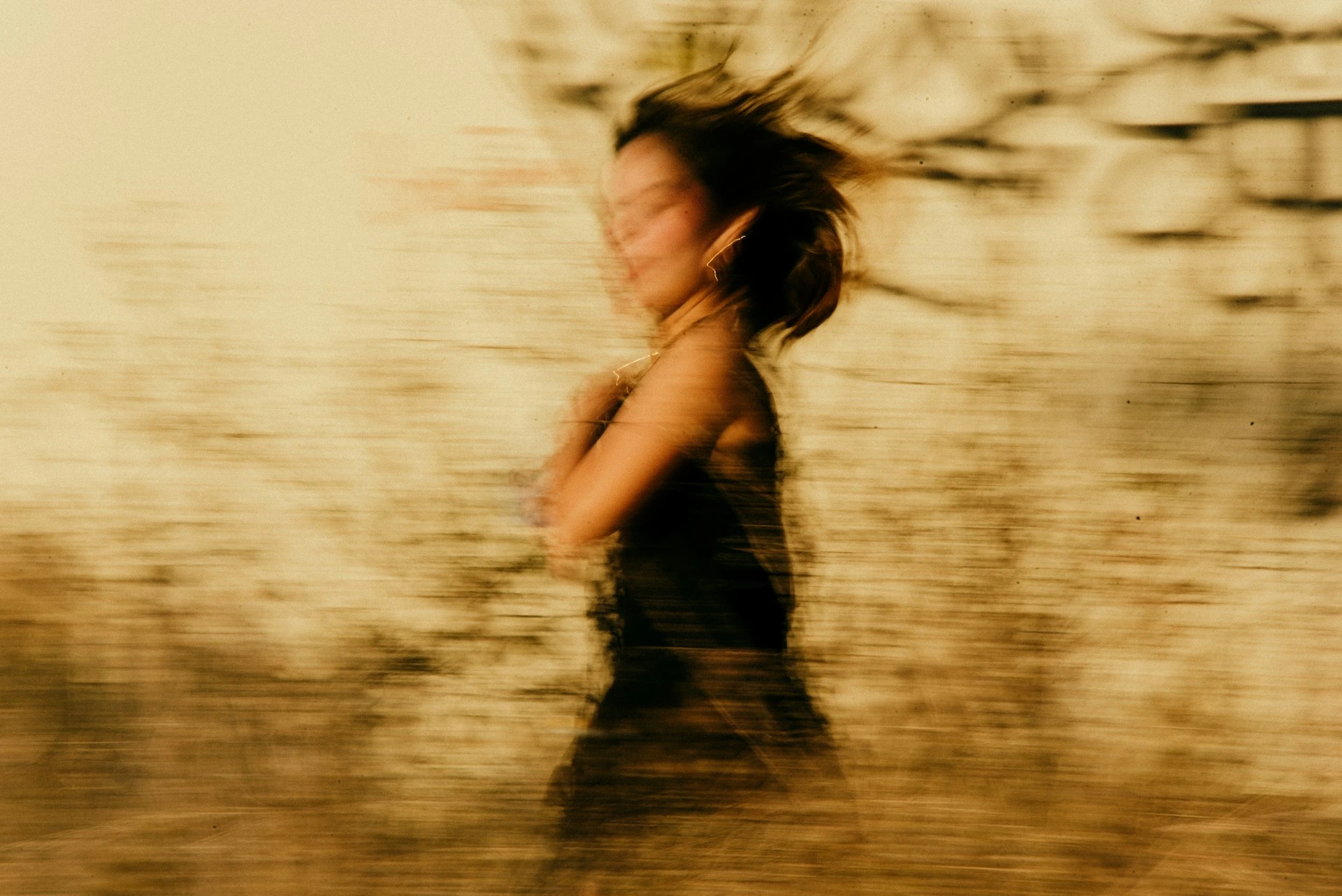 Motion-blurred photo of person running or spinning in warm sepia tones, capturing dynamic movement and energy.
