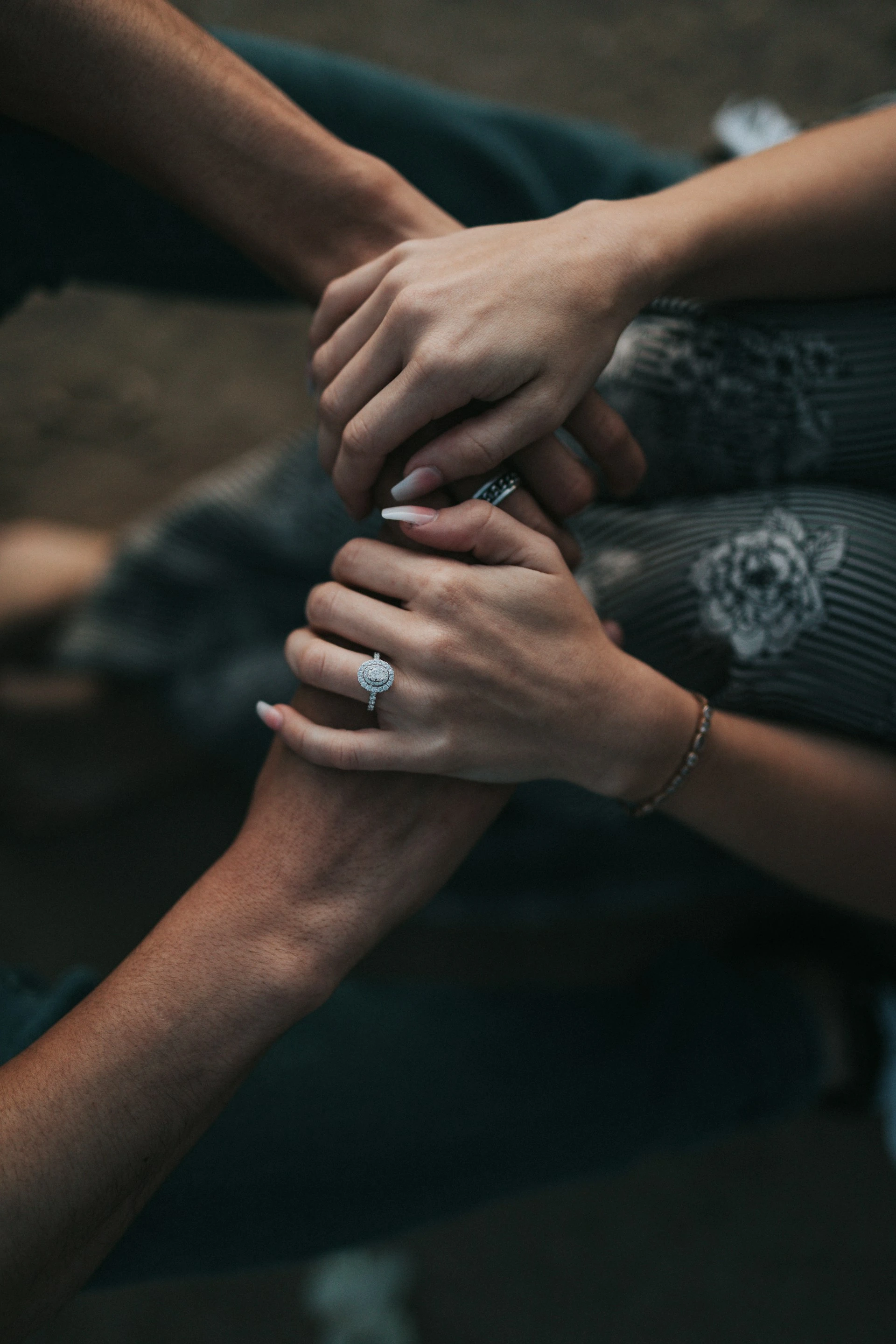 Close-up of two people's hands clasped together, one wearing an engagement ring and the other a dark band, intimate moment.