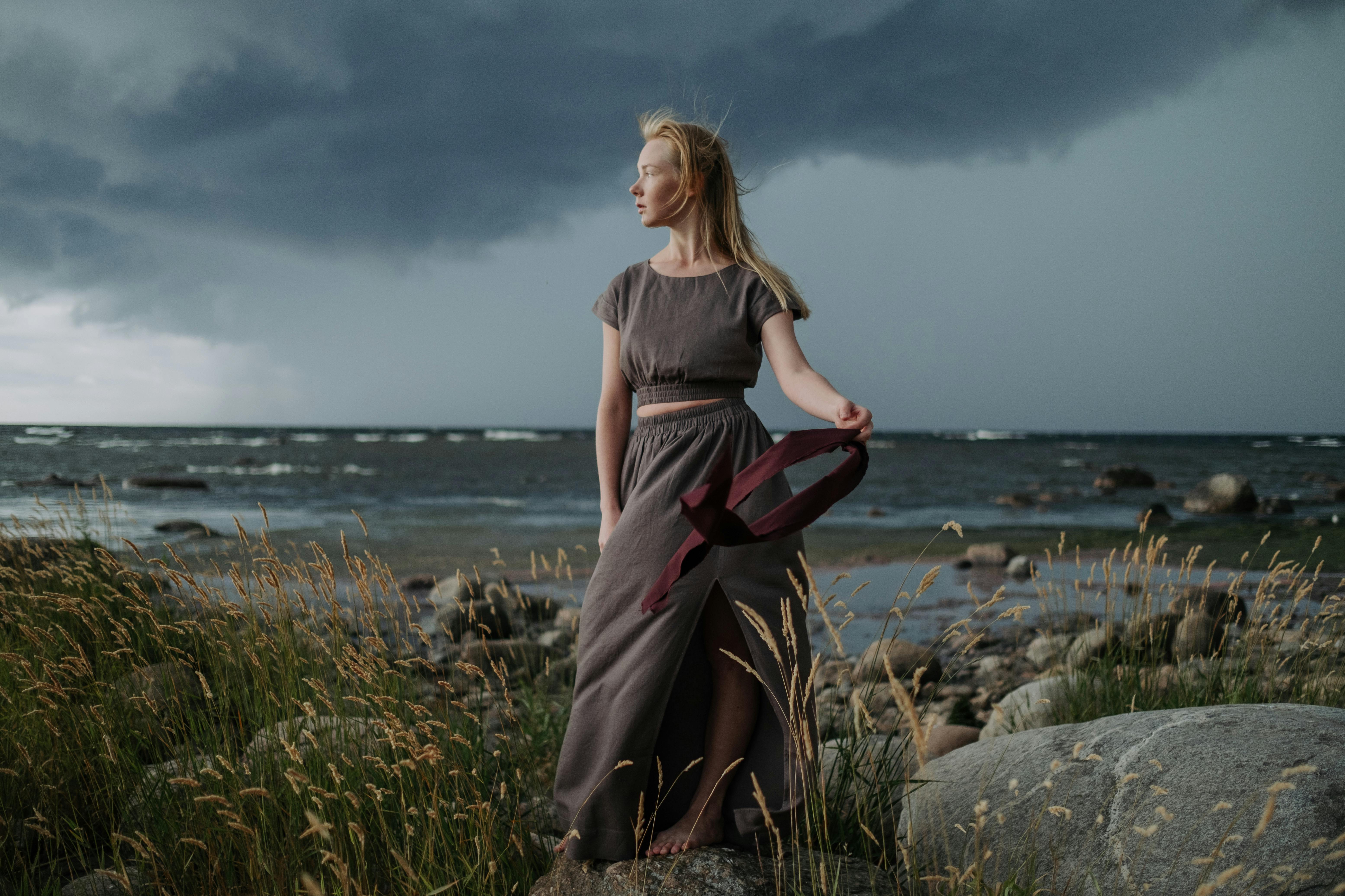 A Woman in Gray Long Dress Standing on Big Rock while Looking Afar