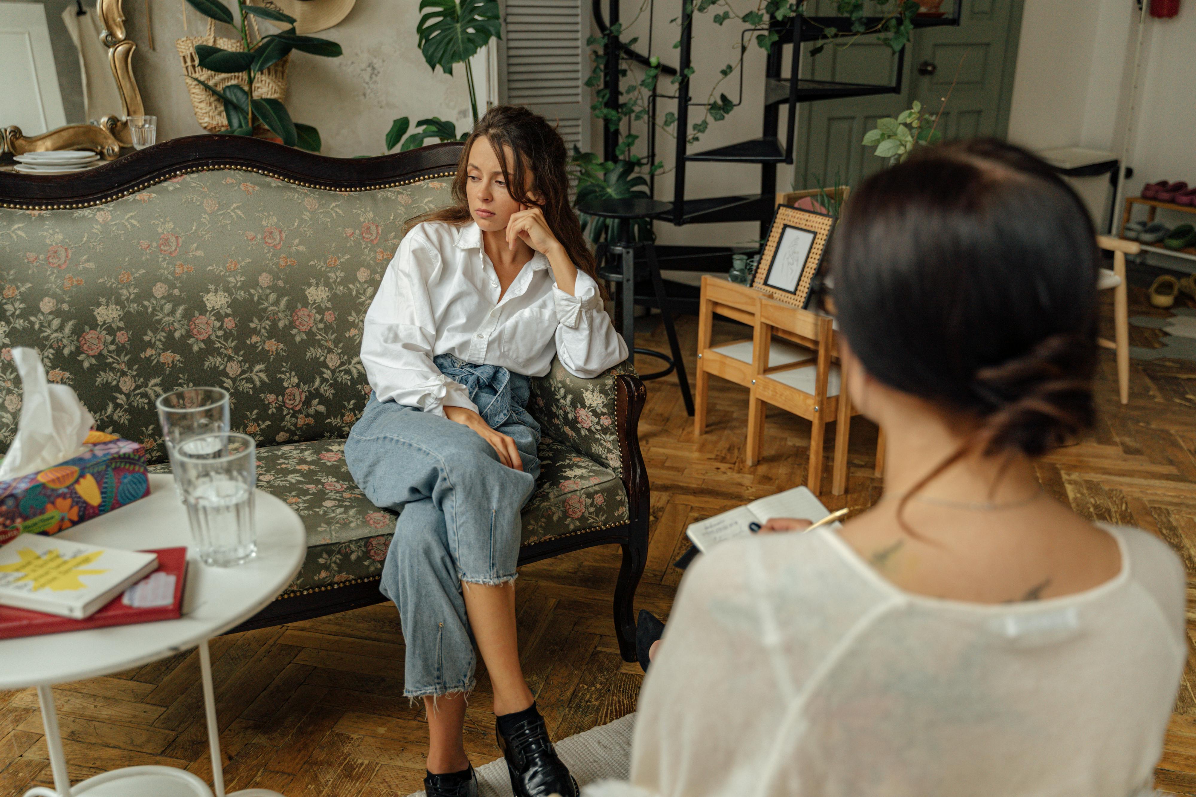 Woman in White Long Sleeve Shirt Sitting on an Antique Loveseat Looking Away From Therapist