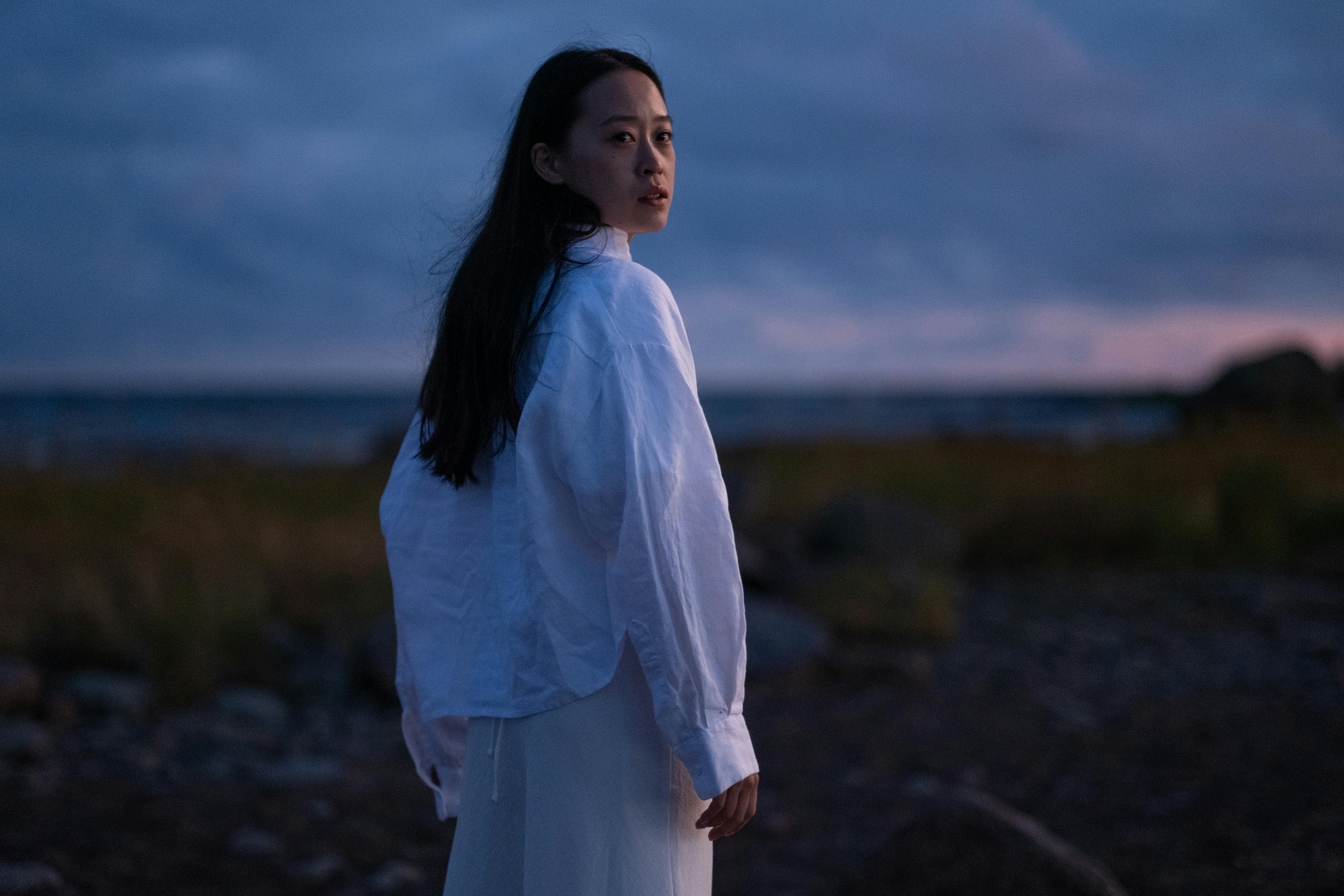 Asian woman framed by a storm clouds hovering over the ocean in the distance. 