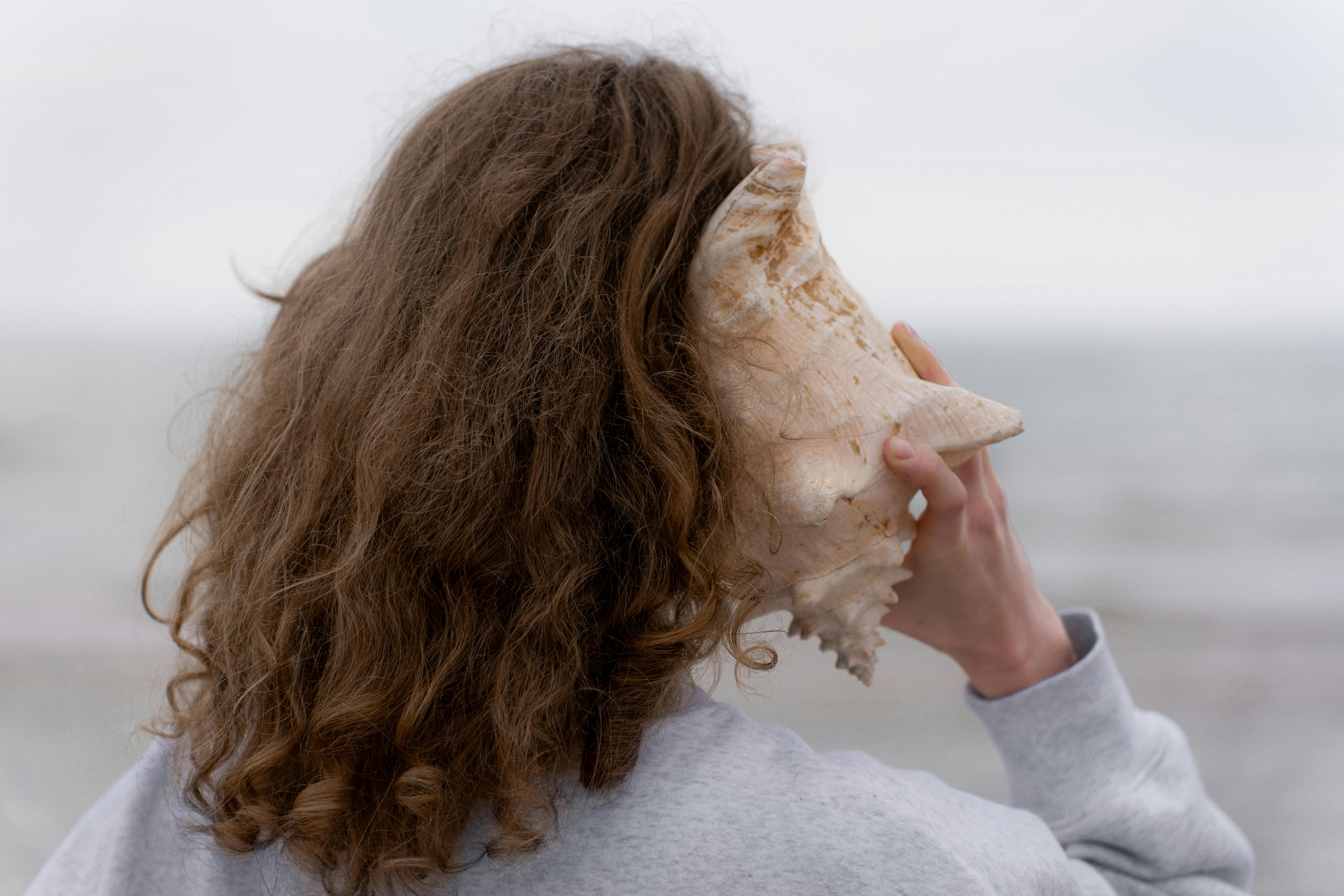 A woman,listening to a large seashell. 