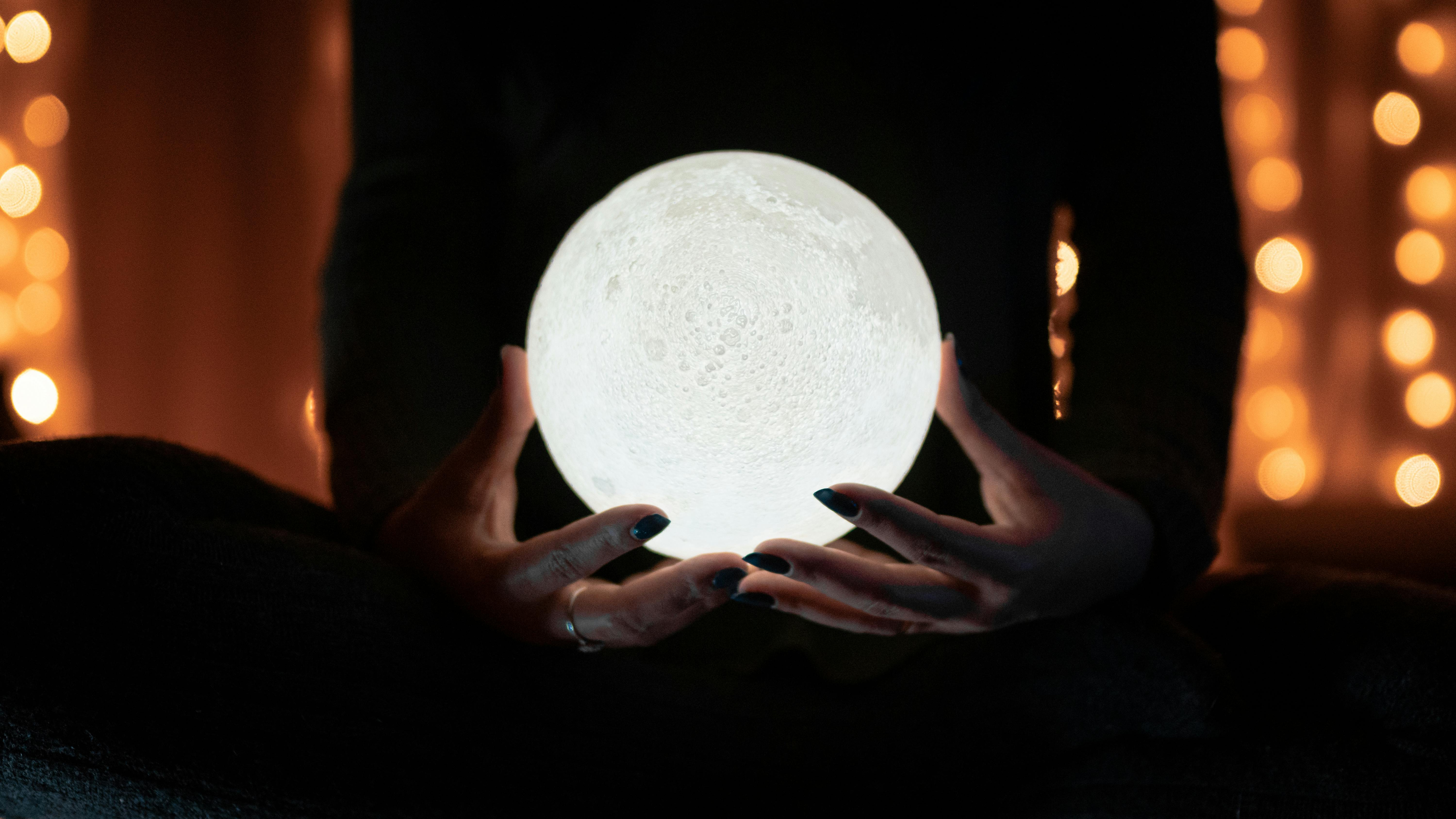 A person holding a globe that looks like the moon. 