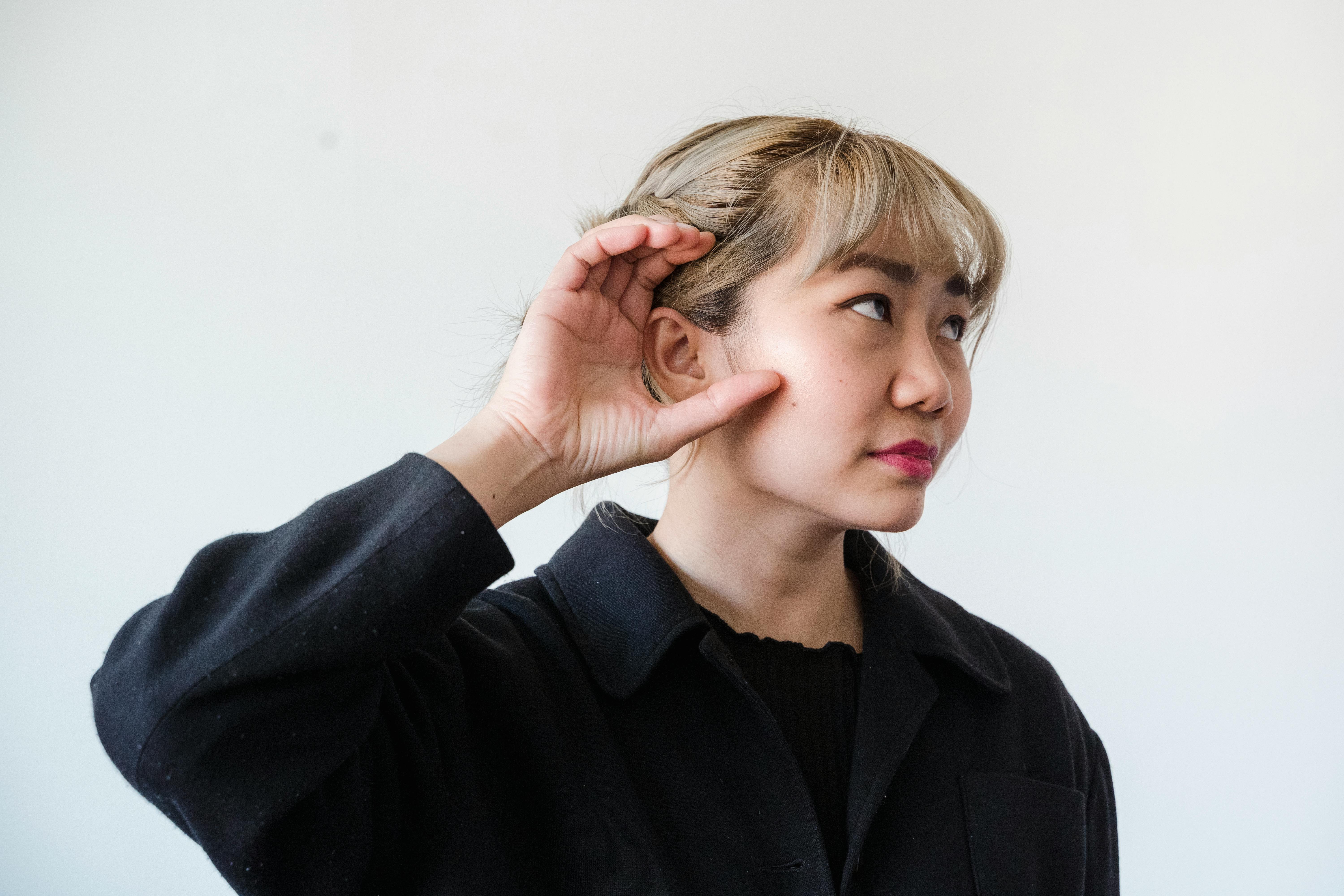 Asian woman cupping her ear to signal speak louder. 