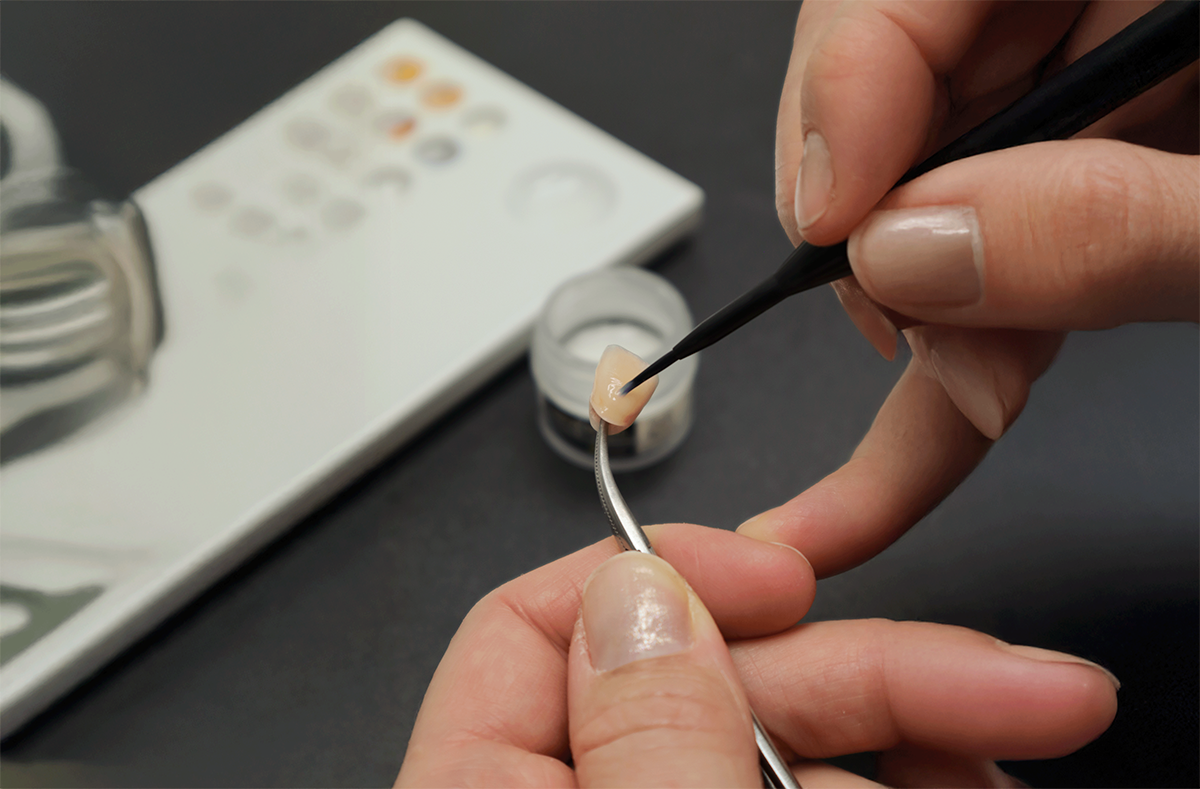 Närbild av två händer som applicerar färg med en pensel på en porslinskrona.