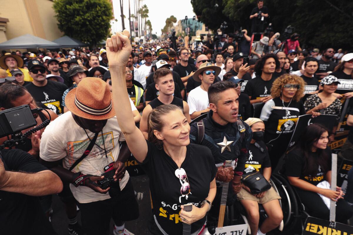 A woman holding up a fist amid a crowd of strikers outside a studio.