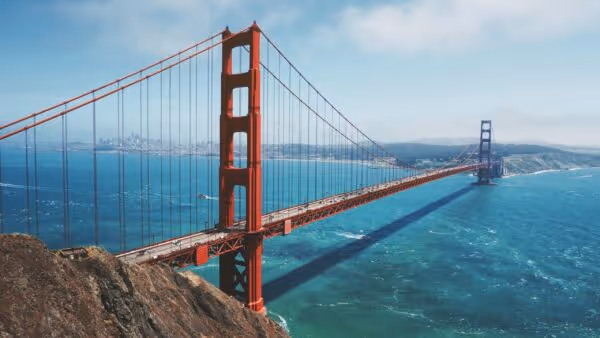 Wide view of the Golden Gate Bridge spanning blue water under a partly cloudy sky.