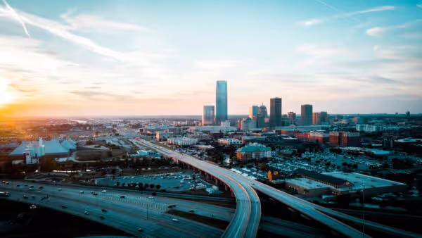 City skyline at sunset with elevated highways curving through urban buildings.