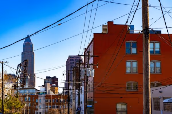 Cityscape with tall buildings and utility poles with many overhead wires against a clear blue sky.