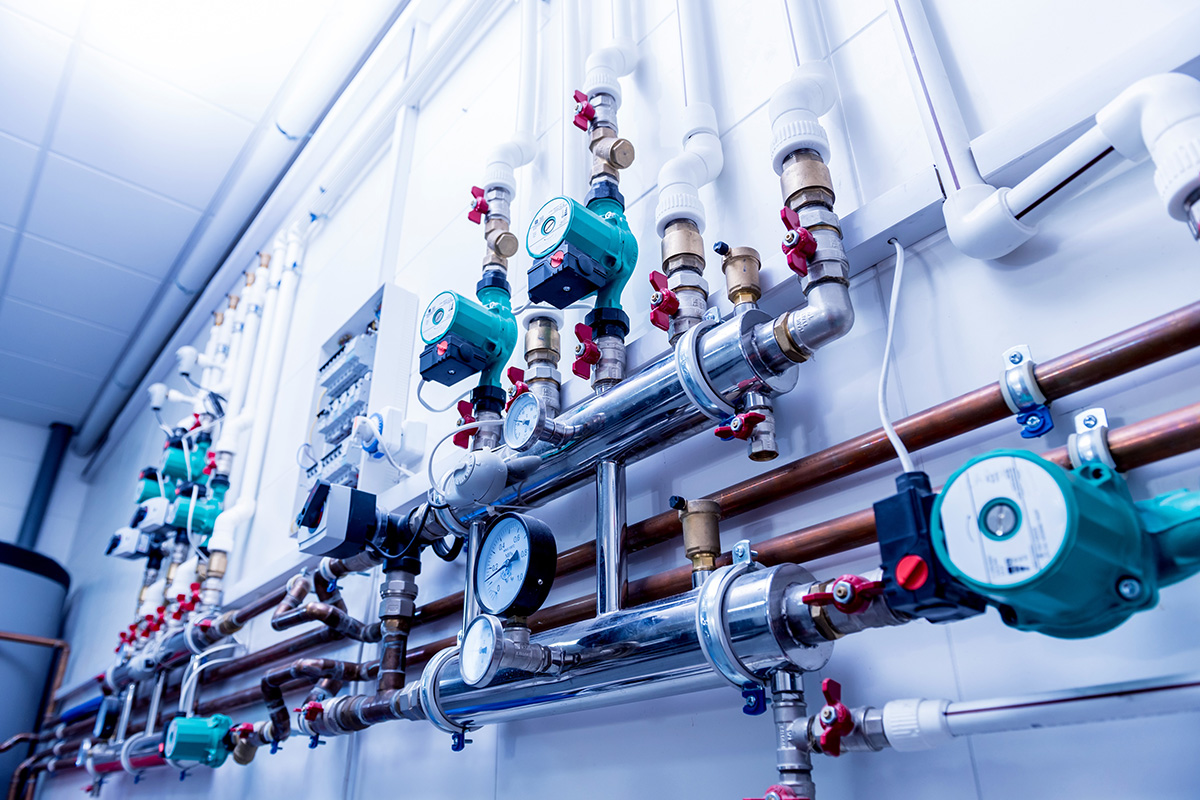 Complex industrial piping system with pressure gauges and green water pump valves mounted on a white wall.