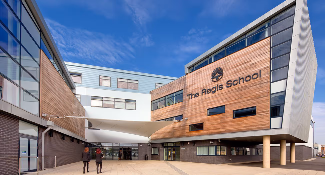 Modern building of The Regis School with wood paneling, large windows, and a white canopy over the entrance area.