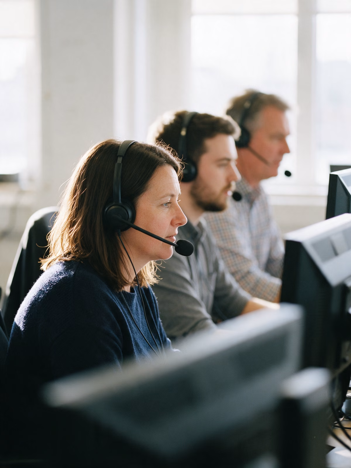 Three colleagues wearing headsets on calls at a row of desks