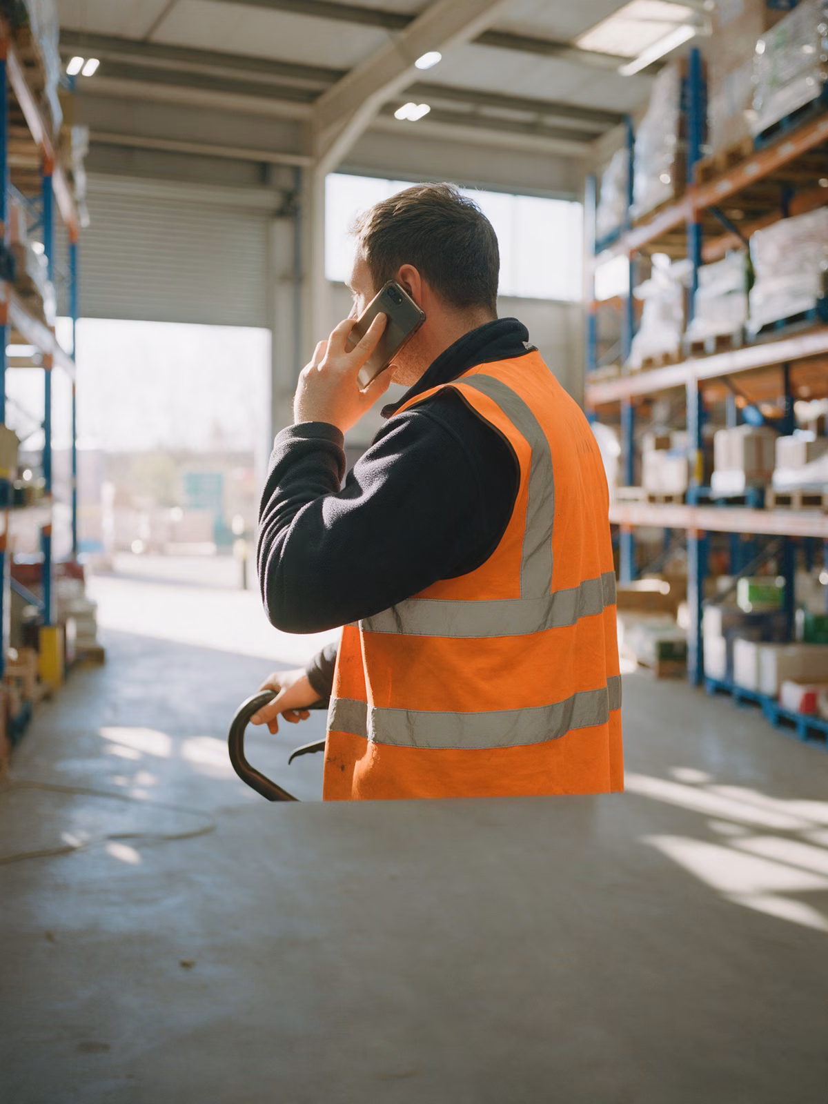 Warehouse worker in a hi-vis vest taking a call on his mobile beside pallet racking
