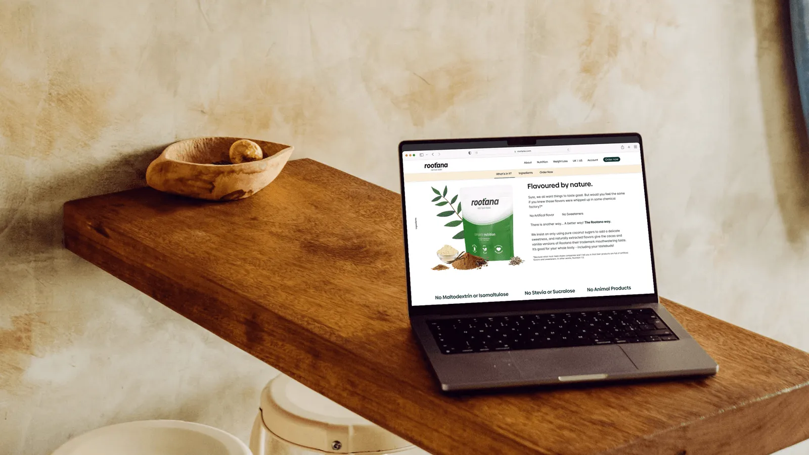Photograph of Macbook featuring Rootana’s website on rustic wooden table, screen shows the unique selling points of the brand