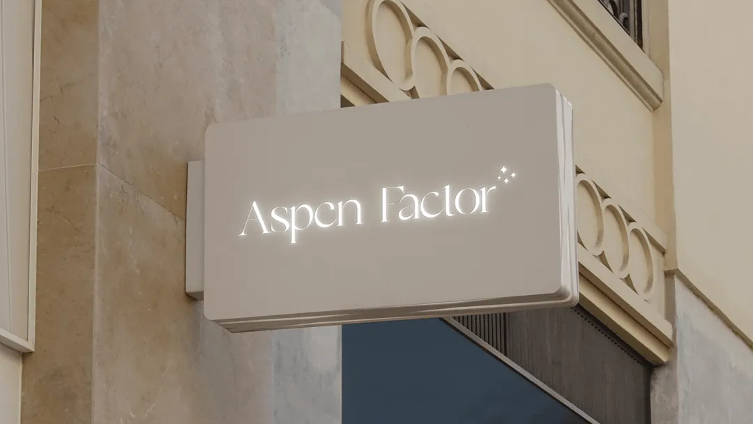 hero image of the Aspen Factor logo on a sign outside the shop attached the the wall; the logo has a white neon effect