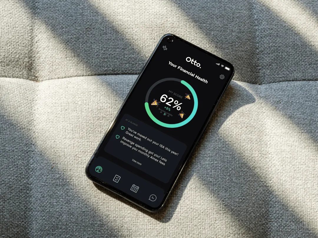 Person sat at a table with a coffee and a notebook holding an iphone with the Otto messaging service open