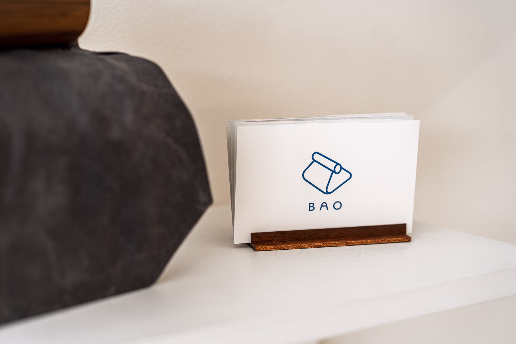 Close-up of a small BAO-branded display card in a wooden holder, showing the BAO logo in blue above the product name.