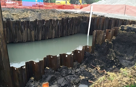 Construction site excavation with wooden retaining walls filled with murky water.